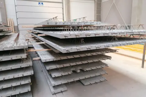 Stos prefabrykowanych płyt betonowych z widocznym zbrojeniem, przypominającym delikatny filigran.