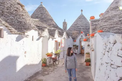 Una donna passeggia tra i trulli di Alberobello, un'icona di cosa vedere in Puglia. Le case coniche e i colori vivaci creano un'atmosfera magica.