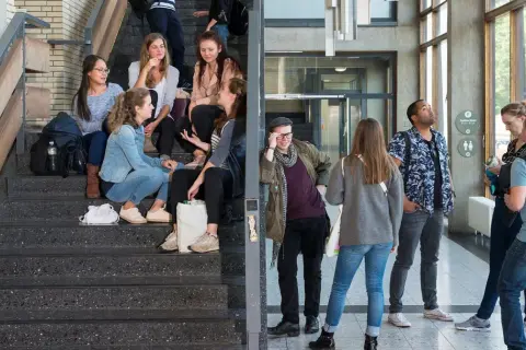 Studenten auf Treppen und im Flur. Eine Gruppe junger Leute, die sich auf einer Treppe unterhalten, vielleicht nach einem Kurs im berufsbegleitenden Studium Berlin.