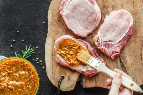 Frisches **Schweinefleisch marinieren** für zarte Steaks. Eine würzige Marinade wird mit einem Pinsel aufgetragen.