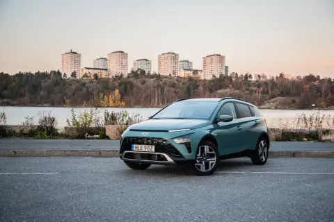 Grön Hyundai Bayon parkerad vid en sjö med stadssiluett i bakgrunden. En perfekt bil för en testkörning i skymningen.