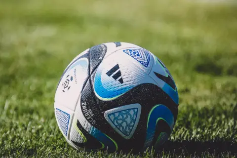 Piłka nożna na zielonej trawie, z widocznymi detalami i logo Adidas.