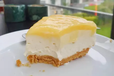 En krämig bit citron cheesecake med krispig botten, redo att avnjutas.