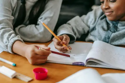 Dos niños concentrados en su dictado de 3 primaria, escribiendo en un cuaderno con lápices.