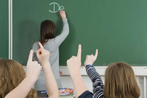 Lehrerin schreibt "De" an Tafel, Schüler heben Hände. Einblick in die bildungspolitik deutschland.