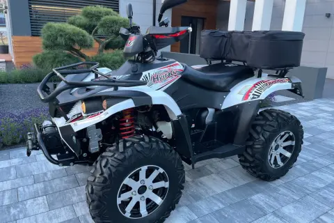 Hyosung TE 450 gotowy na przygodę. Biało-czarny quad z czerwonymi akcentami i bagażnikiem z tyłu.