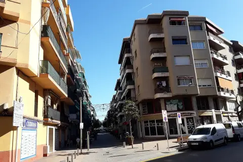 Calle soleada en Les Roquetes del Garraf, con edificios residenciales y comercios.
