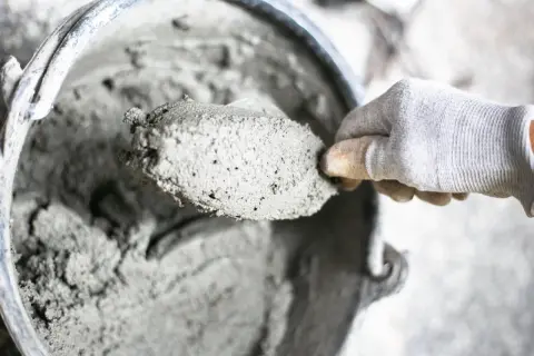Mano guantata raccoglie cemento fresco da un secchio. I materiali leganti sono pronti per l'uso.