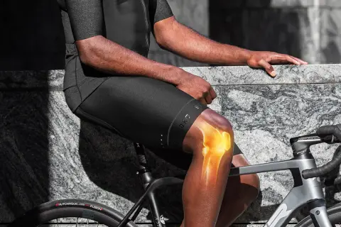 Cycliste ressentant une douleur au genou interne, le genou illuminé pour montrer l'inconfort.