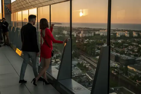 Para na tarasie Olivia Star podziwia zachód słońca nad miastem.