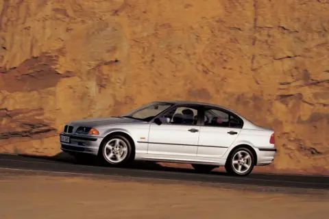 Srebrne bmw e46 330i sunie po drodze na tle skalistego, pomarańczowego zbocza.