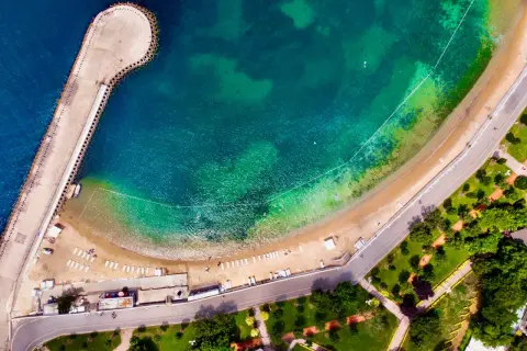 Vista aerea di una spiaggia e di un molo a Istanbul, dove c'è il mare turchese e una strada costiera con un parco verde.