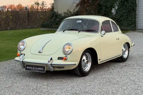 Klasyczny kremowy Porsche 356 z czerwoną tapicerką, zaparkowany na żwirowej nawierzchni.