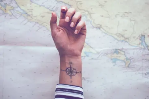 Ein Handgelenk mit einem Kompass-Tattoo, das die Verbundenheit von Geschwistern symbolisiert, vor einer Seekarte.