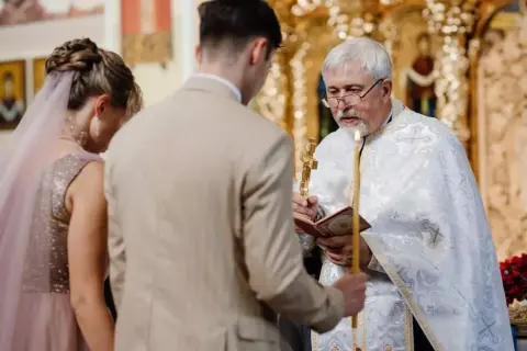 Para Młoda klęczy przed kapłanem podczas cichego ślubu kościelnego bez mszy. Kapłan trzyma krzyż i świecę.