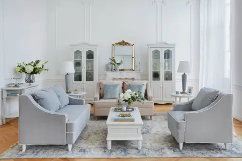 Salotto in stile shabby con divani grigi, poltrone, tavolino bianco, specchio dorato e vetrine.