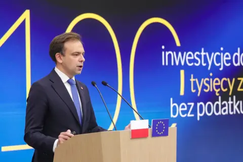 Mężczyzna w garniturze przemawia za mównicą. Na ekranie za nim napis: "inwestycje do tysięcy zł bez podatku".