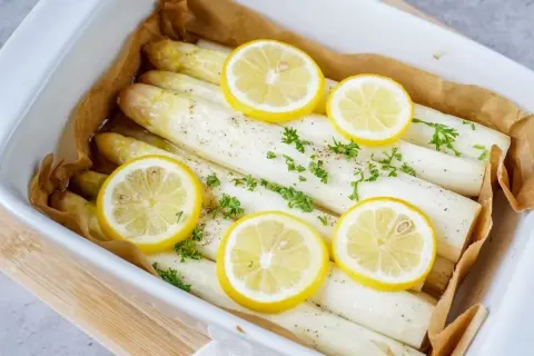 Frischer weißer Spargel im Backofen mit Zitronenscheiben und Petersilie, bereit zum Genießen.