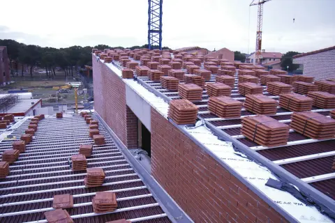 Pilotes de tejas rojas apiladas en la cubierta de una casa en construcción. Grúas en el fondo.