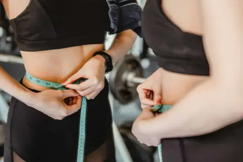 Donna in palestra misura la vita con un metro, segno di un percorso di dimagrimento.