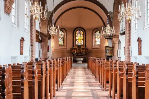 Wnętrze świątyni protestanckiej z rzędami drewnianych ławek, witrażami i ozdobnymi żyrandolami.