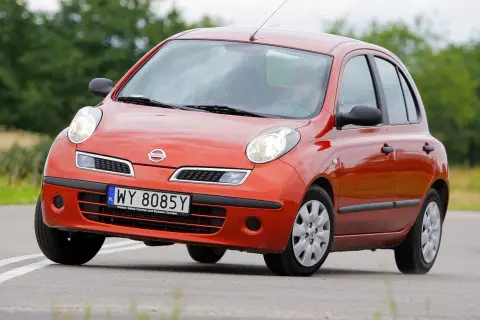 Pomarańczowy Nissan March z tablicą rejestracyjną WY 8085Y jedzie po drodze wśród zieleni.