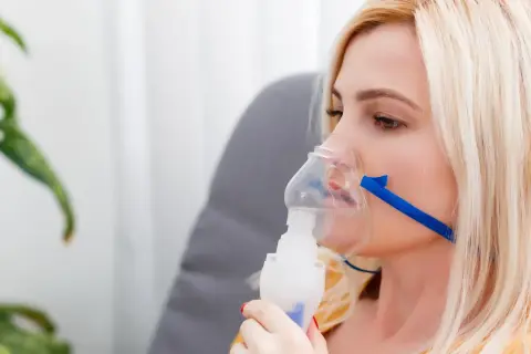 Kobieta z maską nebulizatora, wdychająca sól fizjologiczną.