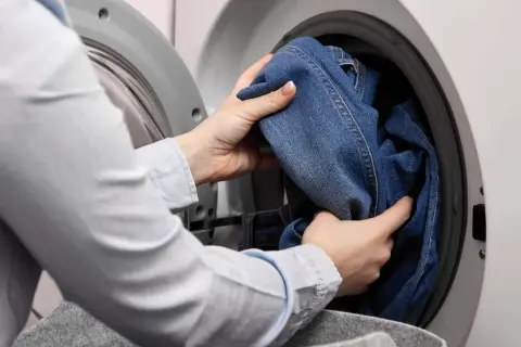 Hände legen Jeans in die Waschmaschine. Das passende Jeans waschen Programm wird ausgewählt.