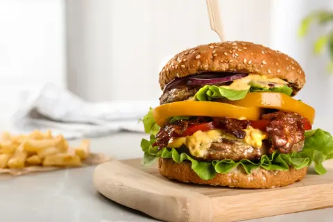 Soczysty burger z wołowiny z dodatkami na desce, obok frytki.