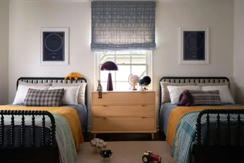 Twin beds with colorful quilts and star charts create fun boys bedroom ideas. A wooden dresser holds globes and a lamp.