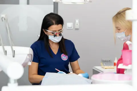 Dentystka w okularach powiększających i masce pracuje nad pacjentem, który odczuwa drętwienie po znieczuleniu zęba.
