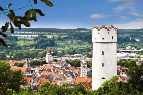Der weiße Mehlsack Ravensburg ragt über die roten Dächer der Stadt. Im Hintergrund grüne Hügel und blauer Himmel.