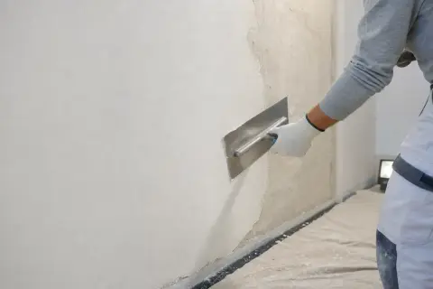 Lavoratore con spatola effettua rasatura muro esterno con rete, creando una finitura liscia e uniforme.
