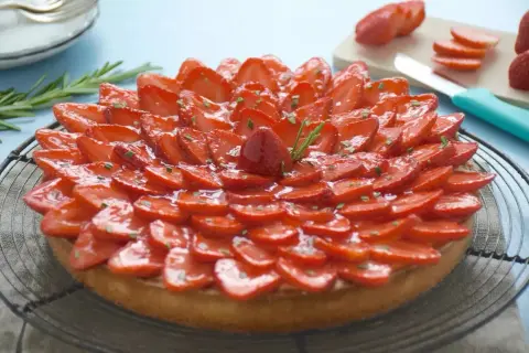 Une magnifique tarte aux fraises, garnie de fraises fraîches tranchées et glacées, décorée de romarin. Un délice visuel et gustatif.