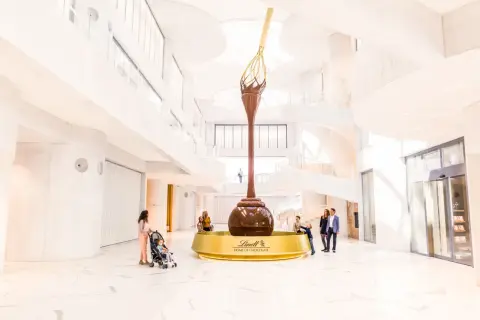 Imponerande chokladfontän i Lindt Home of Chocolate-museet. Familjer beundrar den gigantiska skulpturen i den ljusa, moderna byggnaden.