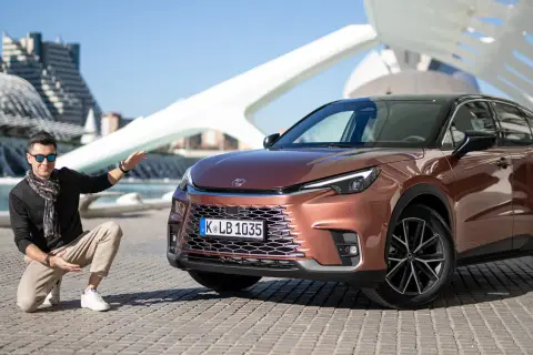 Mężczyzna prezentuje nowy Lexus LBX, zbierając pierwsze opinie. Stylowy SUV w miedzianym kolorze na tle nowoczesnej architektury.