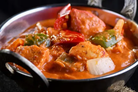 Delicioso pollo al curry con leche de coco, pimientos y cebolla en un cuenco metálico.