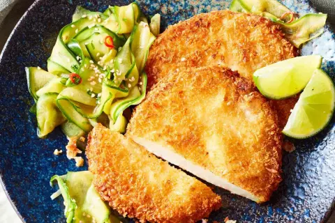 Knuspriges Kohlrabi-Schnitzel mit Gurkensalat und Limettenspalten auf einem blauen Teller.