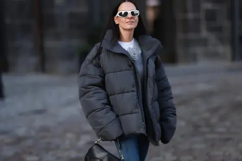 Frau mit Daunenjacke, die sie ohne Trockner wäscht, trägt weiße Sonnenbrille und schwarze Tasche.