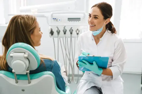 Uśmiechnięta dentystka omawia z pacjentką efekty leczenia aparatem ortodontycznym.