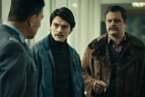Trzech mężczyzn w rozmowie, jeden w mundurze. Atmosfera napięcia, jak w filmie "Hiacynt".