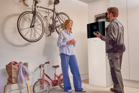 Técnico explica a una mujer el **rendimiento estacional aerotermia** junto a una unidad Daikin. Bicicletas colgadas al fondo.