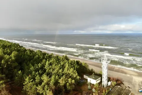 Plaża Kąty Rybackie z wieżą widokową i lasem sosnowym. Na niebie tęcza.
