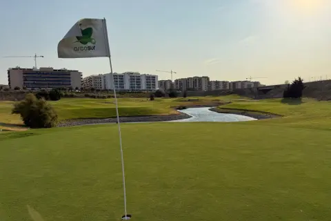 Bandera de Arcosur en un campo de golf, con edificios residenciales y grúas de construcción al fondo.