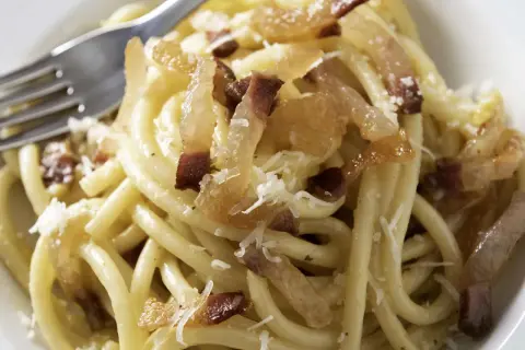 Ein Teller Pasta mit knusprigen Speckwürfeln, die zeigen, was ist Guanciale: luftgetrockneter Schweinebackenspeck, der für den authentischen Geschmack sorgt.