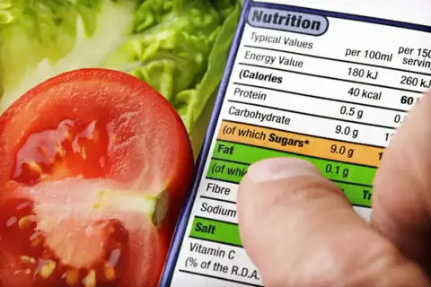 Pomidor i sałata na tle etykiety z wartościami odżywczymi, gdzie palec wskazuje na pozycję "Calories" (kaloria).
