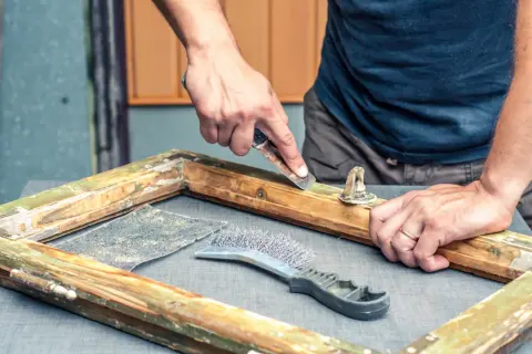 Restaurando un marco de madera, se usa una rasqueta para decapar madera vieja y pintura descascarada.