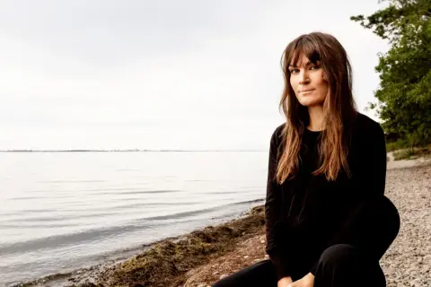 Malin Wollin sitter vid en stenig strand med havet i bakgrunden.