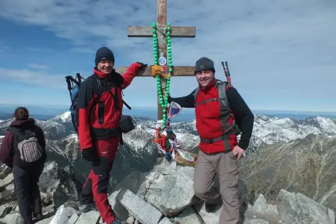 Dwóch turystów na szczycie w Tatrach Wysokich 2494 m, przy drewnianym krzyżu ozdobionym zielonymi paciorkami.
