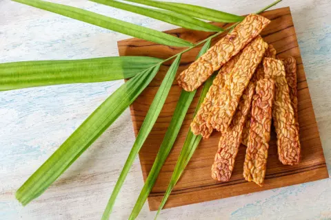Knusprige Tempeh-Sticks auf einem Holzbrett, garniert mit grünen Blättern. Ein leckeres Tempeh-Rezept für gesunde Ernährung.